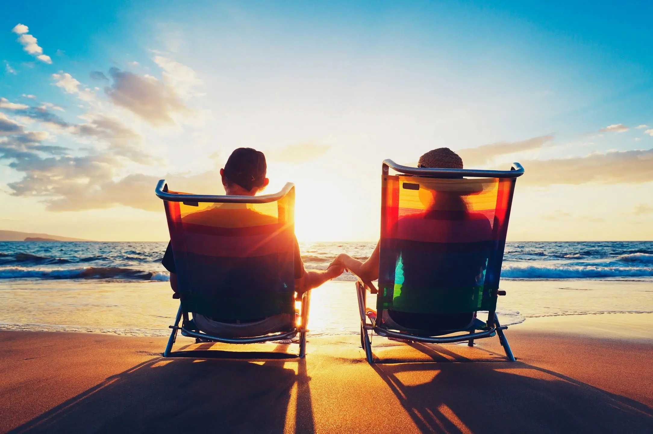 Couple holding hands in beach chairs at sunset