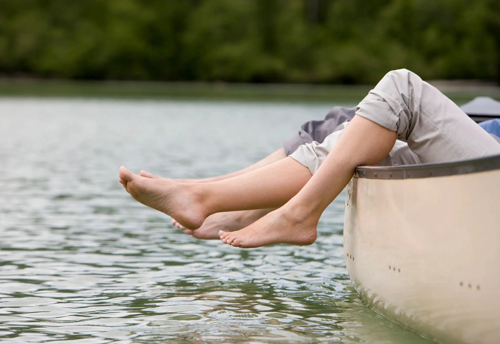 Bare feet dangling from canoe over lake