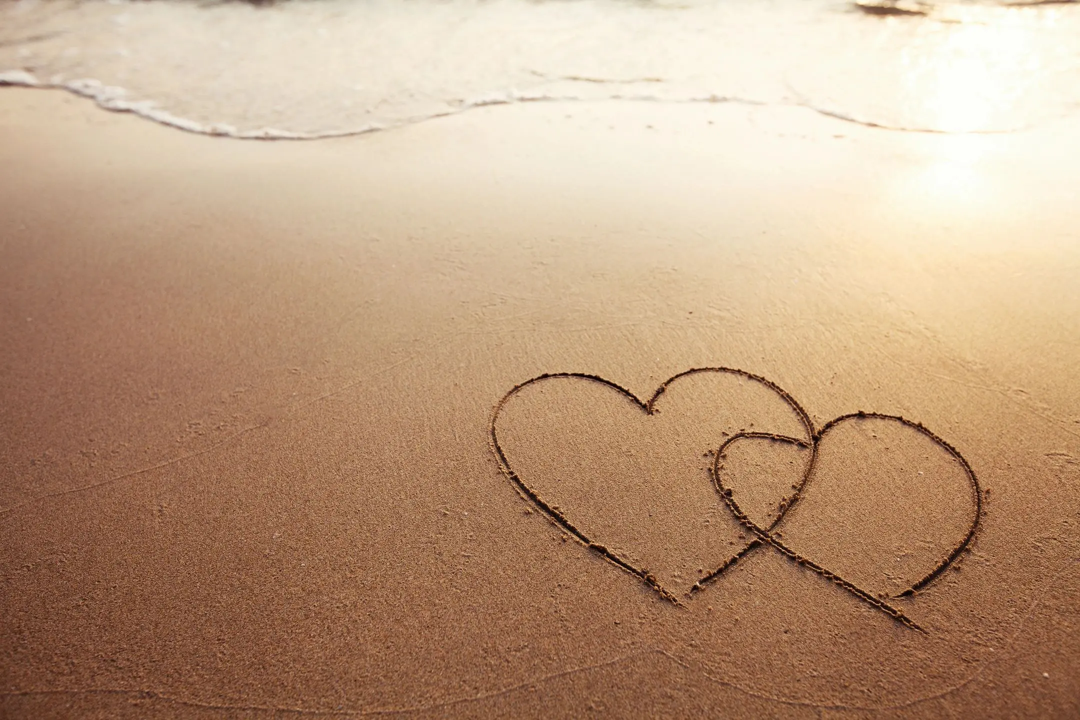 Two intertwined hearts drawn in beach sand