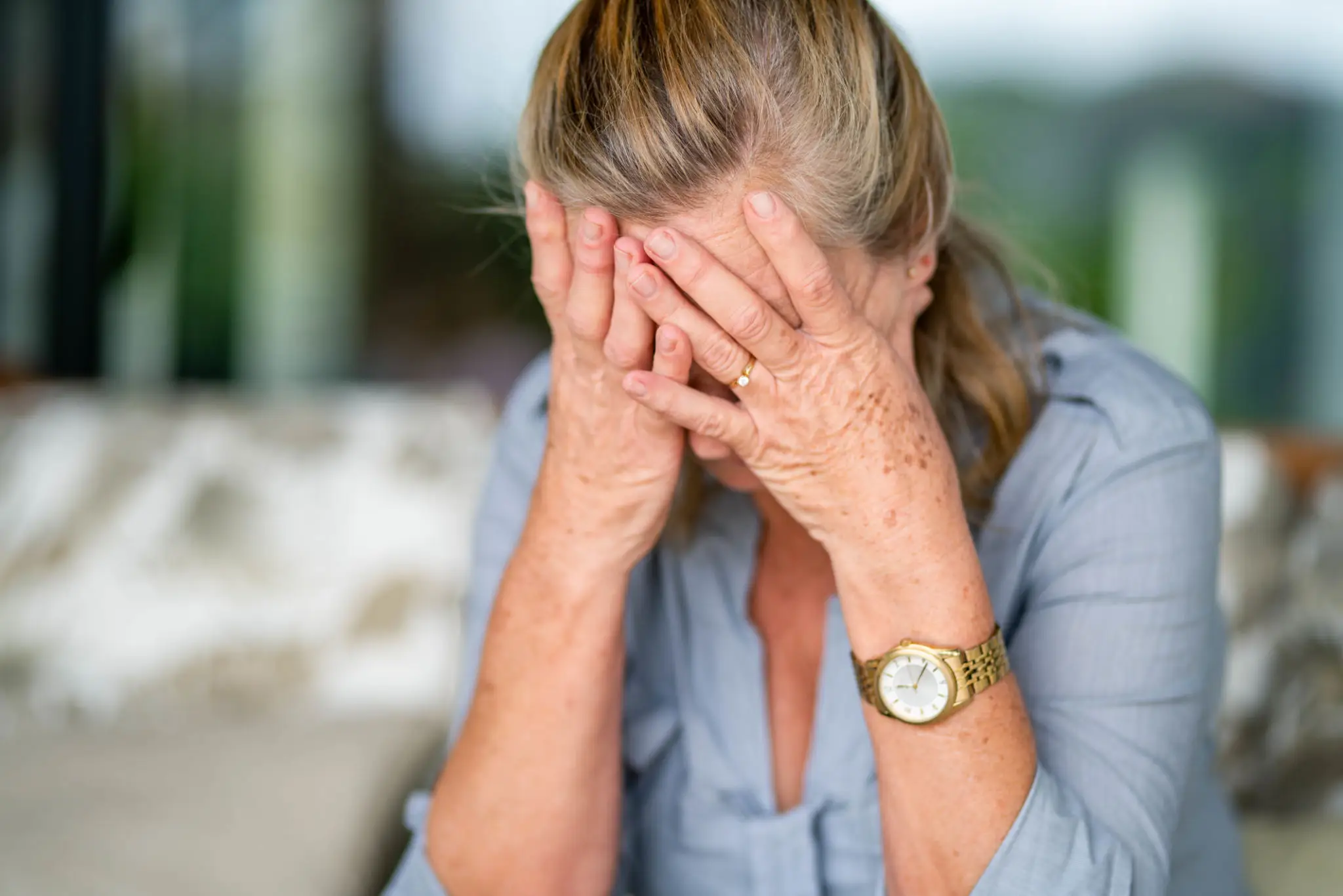 Elderly woman covering her face, appearing distressed.