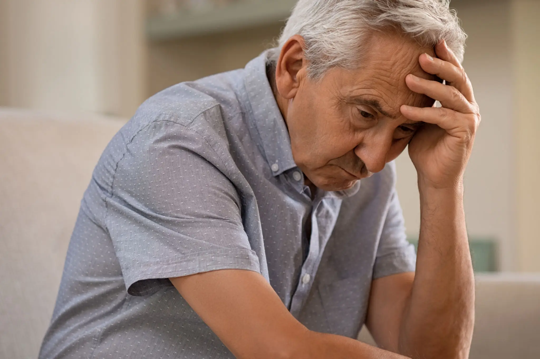 An elderly man looks worried and contemplative, resting his head on his hand.
